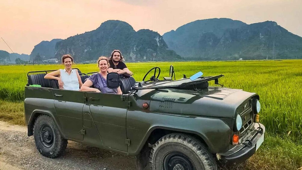 A green jeep parked on a dirt path with a field and mountains in the background. 1