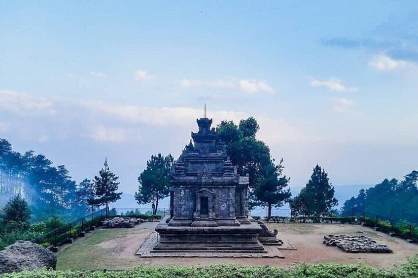 A stone stupa surrounded by a fenced area with trees and a clear sky. 2