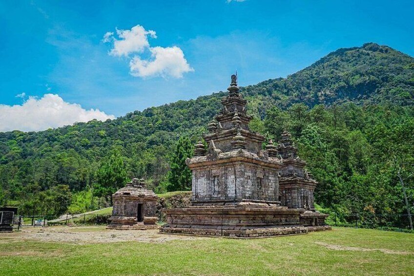 A temple complex with tiered structures, surrounded by lush greenery and a mountain backdrop. 1