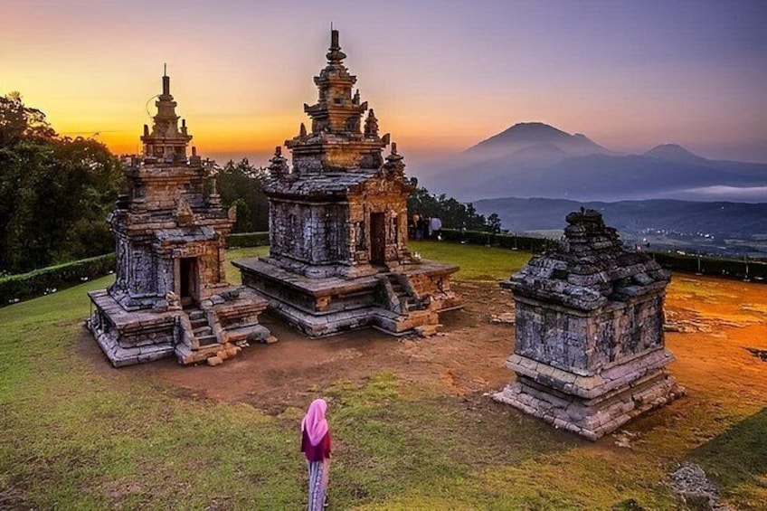 A temple complex with multiple structures, a person in traditional attire, and a mountainous backdrop. 3