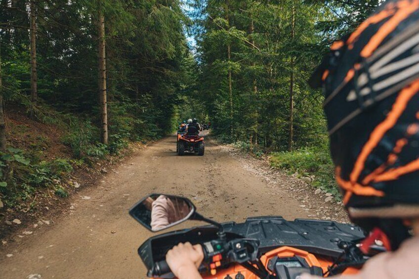 Ein Feldweg, von Bäumen gesäumt, mit einer Person auf einem Quad im Vordergrund und einer weiteren im Hintergrund. 3