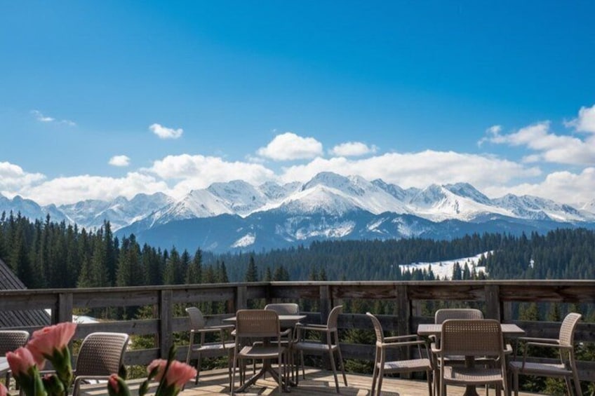 A terrace with chairs overlooking snow-capped mountains and a forested valley. 5
