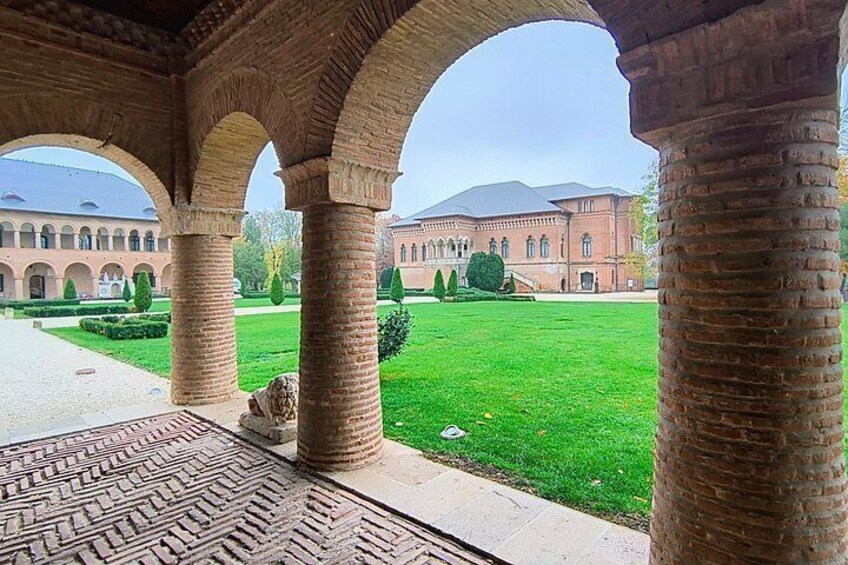 A courtyard with arches, a brick building, and a well-maintained lawn. 5