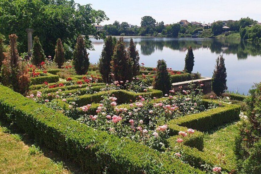 A formal garden with geometrically shaped hedges, flowering plants, and a calm lake. 1