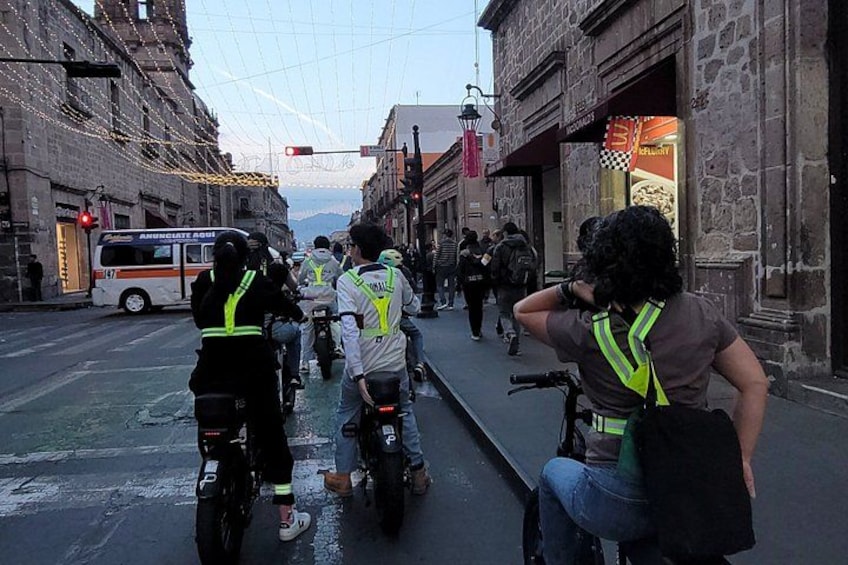 A street with motorcyclists wearing reflective vests, a bus, and pedestrians. 2