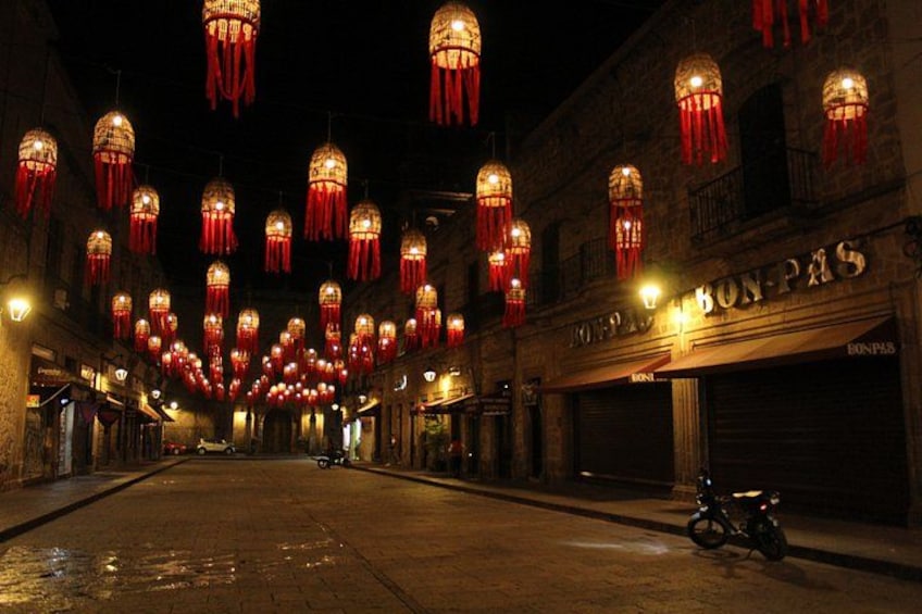 A street at night with red lanterns hanging overhead and a motorcycle parked on the side. 1