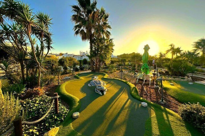 En golfbana med en puttinggreen, palmer och en solnedgång i bakgrunden. 5