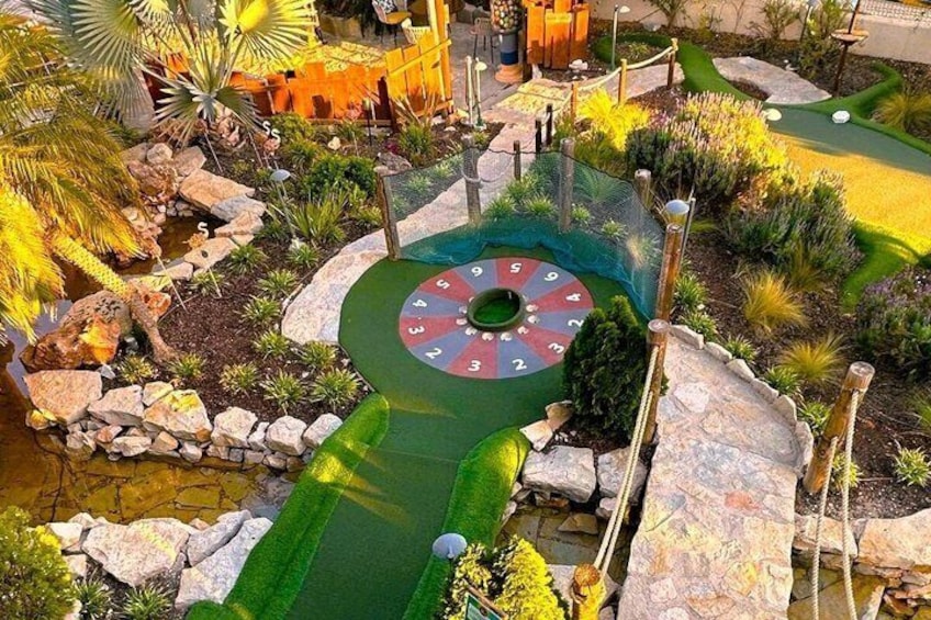 En miniatyrgolfbana med en rund green, ett vattenhinder och omgivande växtlighet. 1