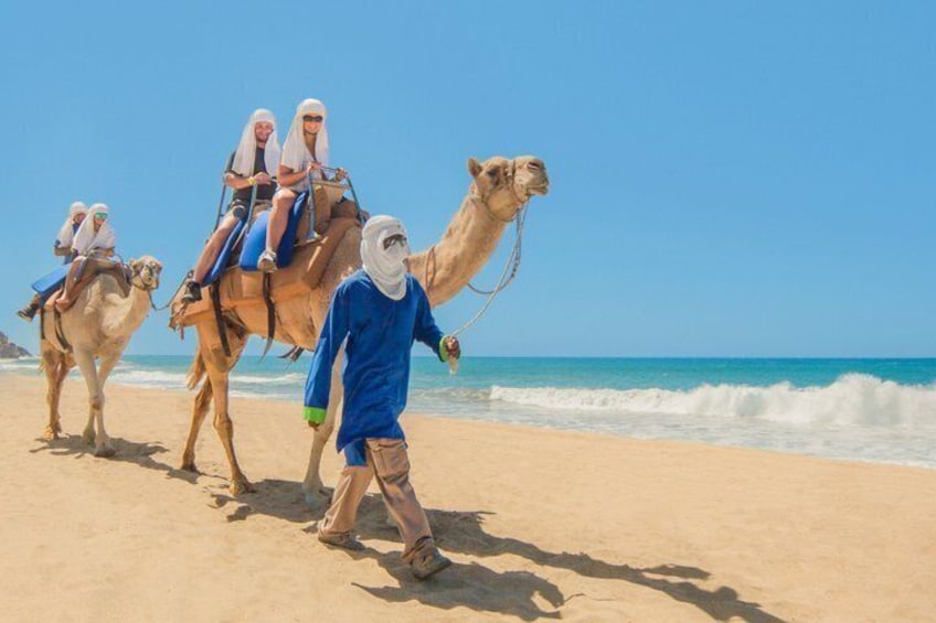 A camel ride on a beach with a person leading the camels. 1