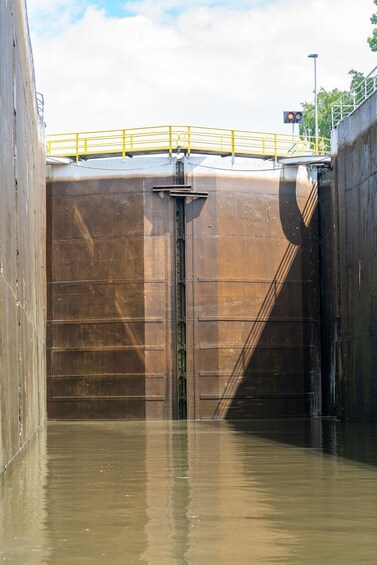 A large industrial lock gate with water flowing through it, surrounded by metal walls and a yellow safety railing. 3