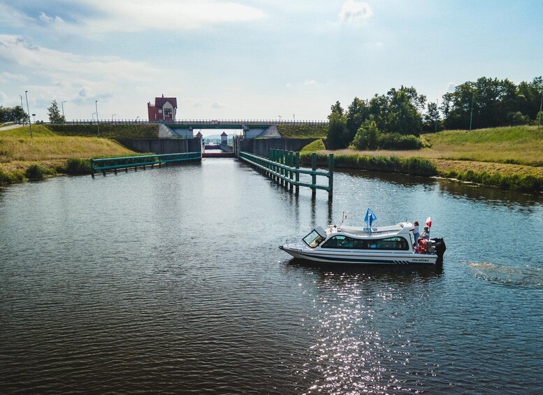 A narrowboat on a canal with a lock ahead, surrounded by greenery and a bridge in the background. 1
