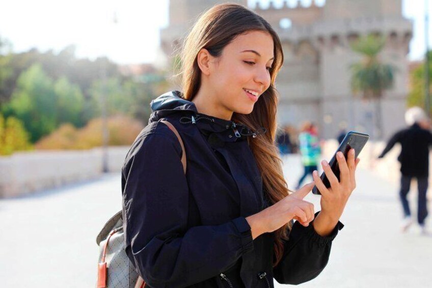 A person using a smartphone, with a backpack and a historic building in the background. 1