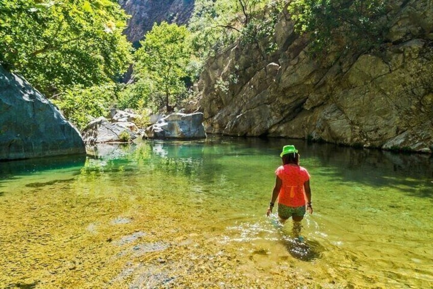 Una persona vadeando un río cristalino rodeado de acantilados rocosos y exuberante vegetación. 5