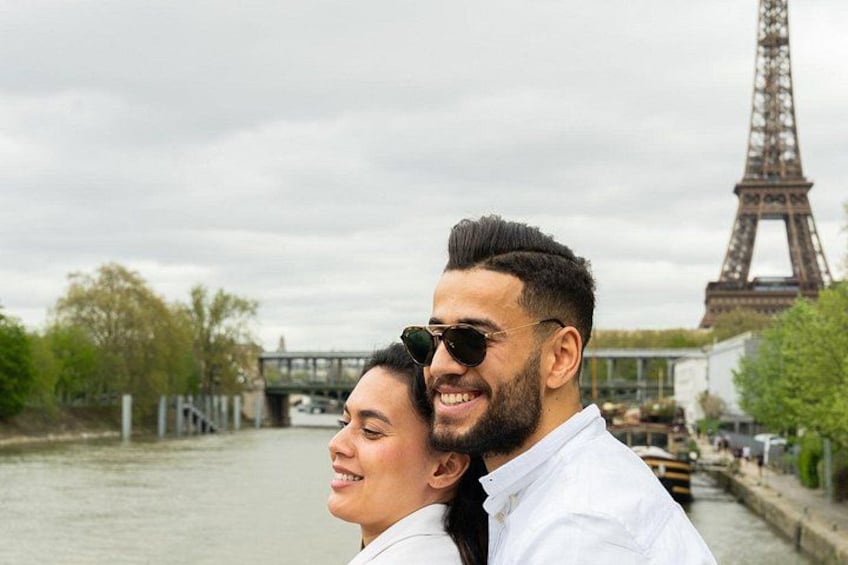 Un couple se tient devant la Tour Eiffel, avec une rivière et un pont en arrière-plan. 2