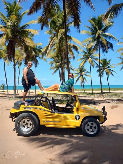 A yellow off-road vehicle on a sandy beach with palm trees and the ocean in the background. 1