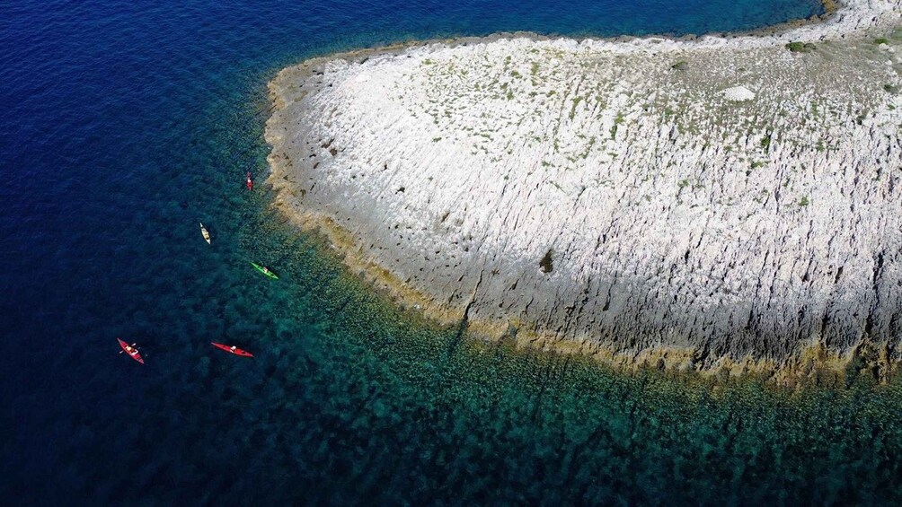 An aerial view of a coastal area with clear waters, rocky shorelines, and kayaks. 4