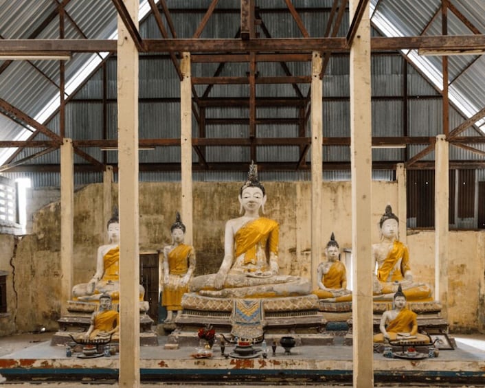 A large Buddha statue surrounded by smaller statues in a temple with a corrugated metal roof. 3