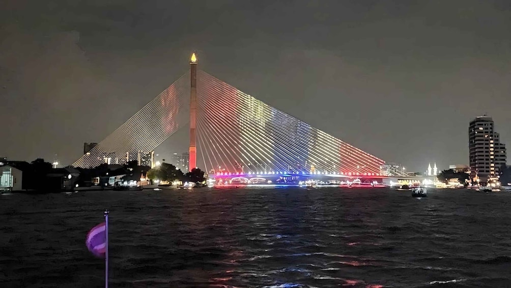 Un puente grande e iluminado con una estructura triangular y una torre en el centro, que cruza un cuerpo de agua. 2