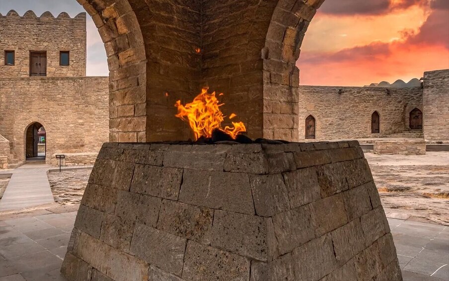 A stone structure with a fire burning inside, surrounded by ancient stone walls and an archway. 1
