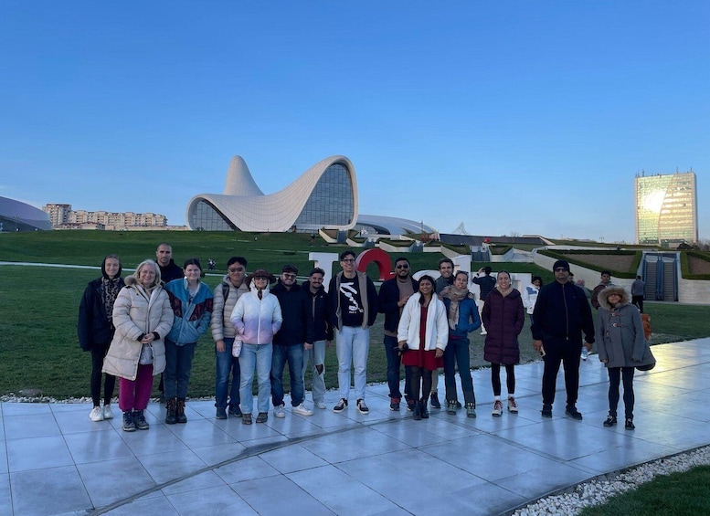 A group of people standing in front of a modern architectural structure with a unique curved design, set against a clear sky. 5