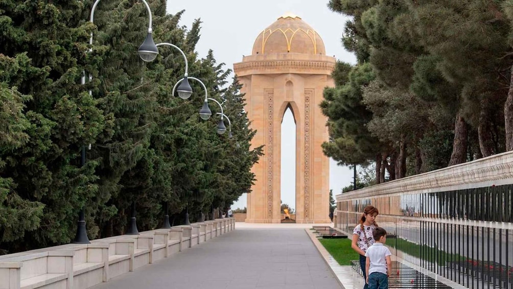 A pathway lined with trees and street lamps leading to a large, domed building with an arched entrance. 4