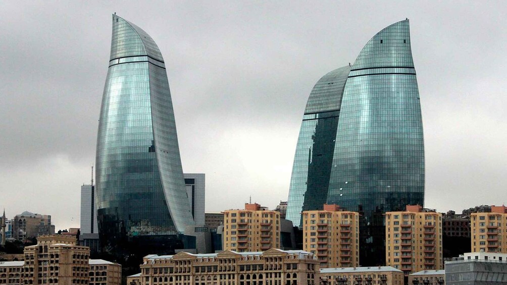 Two modern glass skyscrapers with curved designs, surrounded by older residential buildings. 3