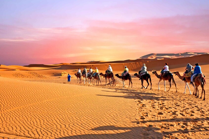 Un grupo de personas cabalgando camellos a través de un paisaje desértico con dunas de arena. 1