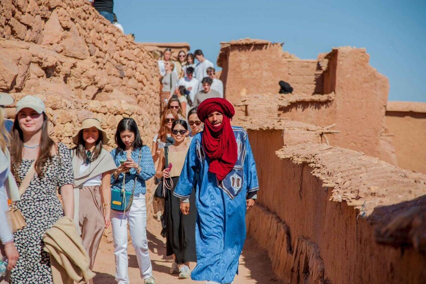 Un grupo de personas camina por un sendero estrecho y pedregoso flanqueado por edificios de adobe tradicionales. 5