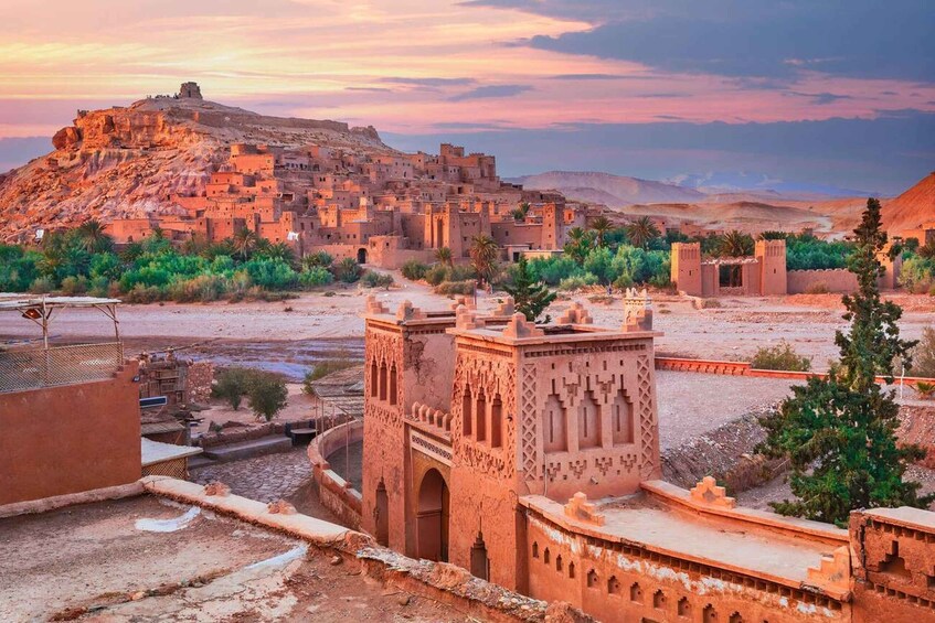 Paisaje desértico con un pueblo fortificado histórico, un alminar destacado y una montaña al fondo. 4