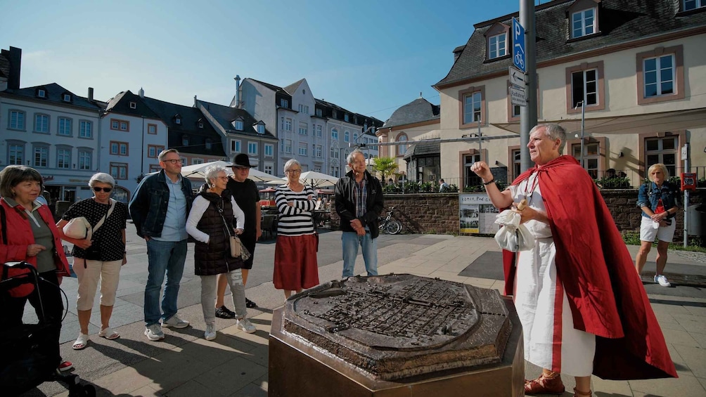 A group of people standing around a historical artifact in an outdoor setting with buildings in the background. 2