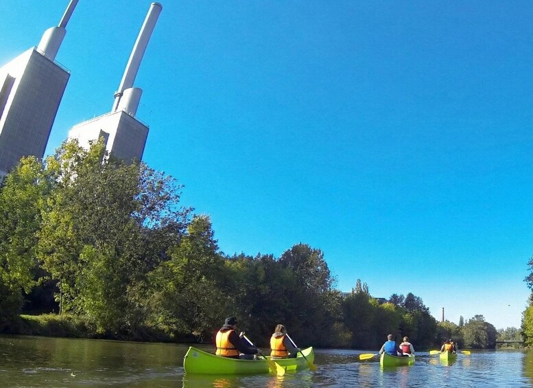 People kayaking on a river with industrial buildings in the background. 3