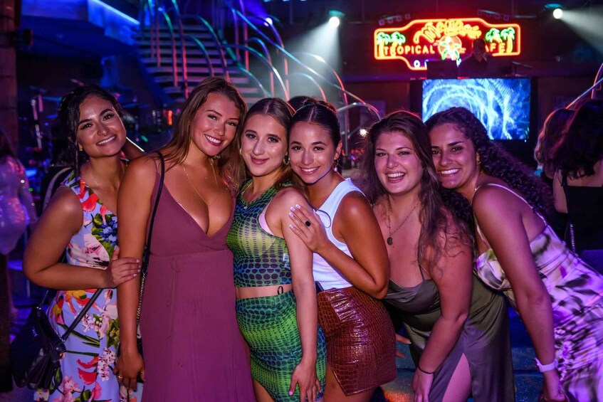 A group of people at a nightclub with neon signs and a staircase in the background. 5