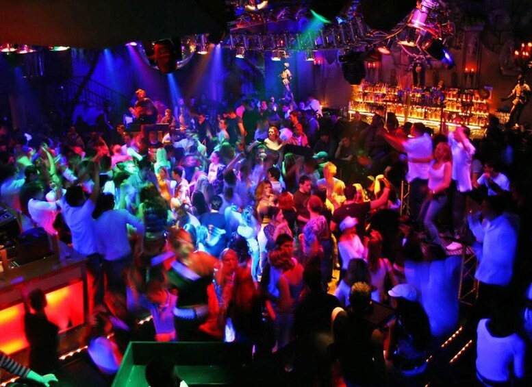 A crowded nightclub with people dancing and a DJ booth in the background. 3