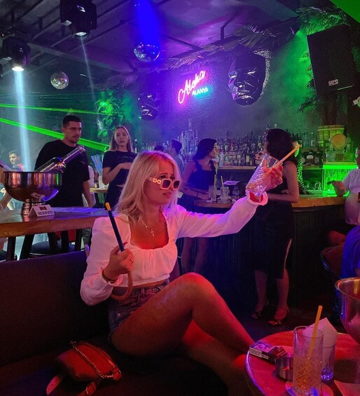 A person seated at a bar with a neon sign in the background. 4