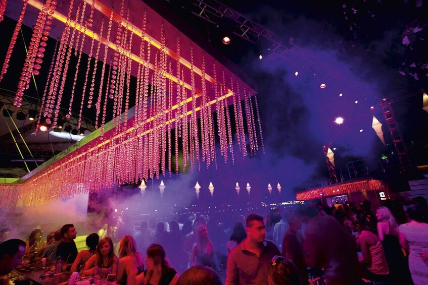 A crowded indoor venue with hanging lights and smoke effects. 2
