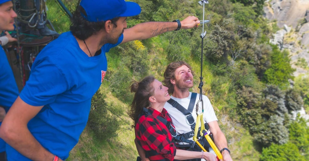 A person in a blue shirt and red plaid shirt preparing for a zip-lining activity with safety harnesses and a guide. 4