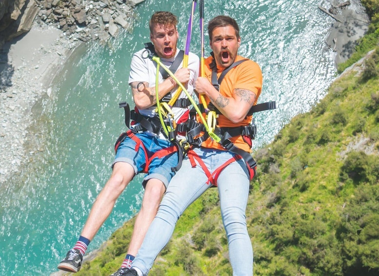 Two people bungee jumping with safety harnesses, overlooking a river and rocky terrain. 5