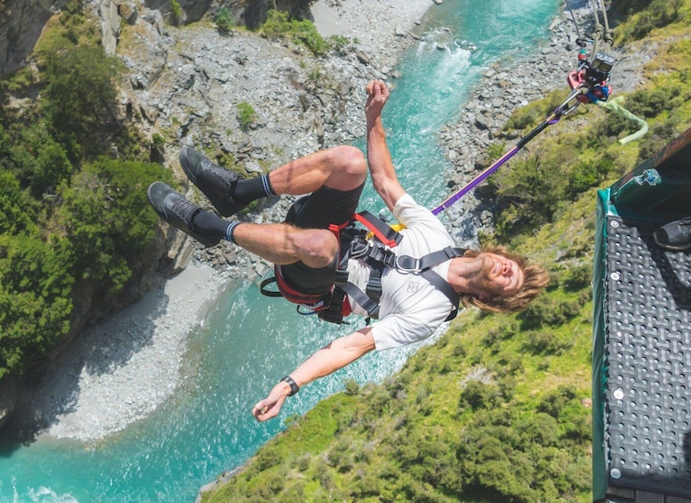 A person bungee jumping with a harness and safety gear, overlooking a river and rocky terrain. 2