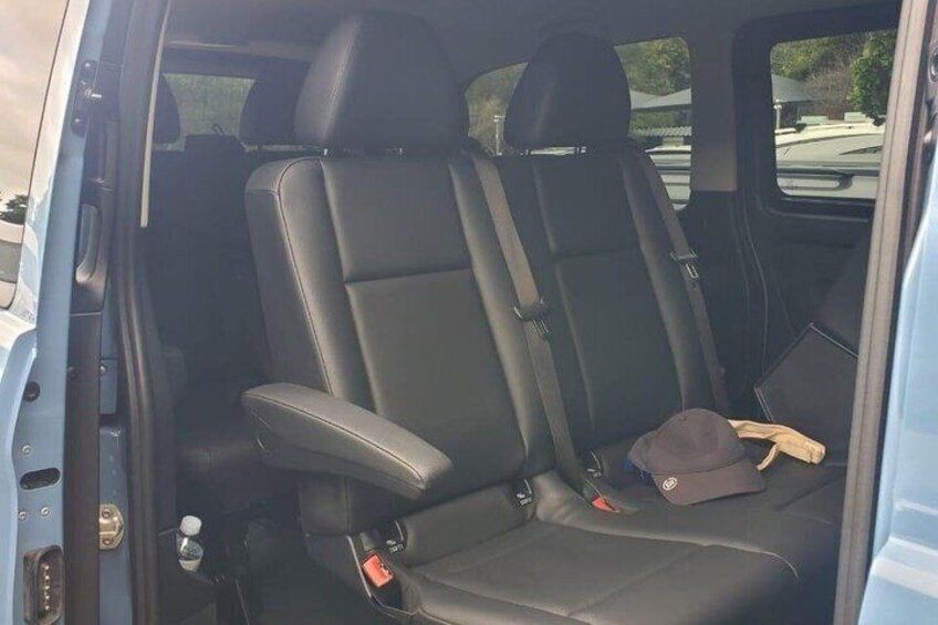 A vehicle interior with black leather seats, a seatbelt, and a hat on the passenger seat. 3