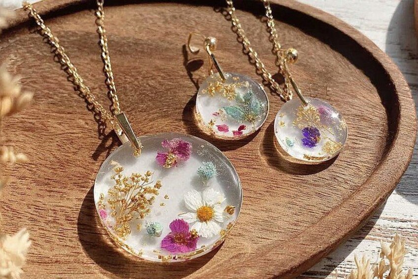 Tres collares colgantes con diseños florales sobre una bandeja de madera. 3