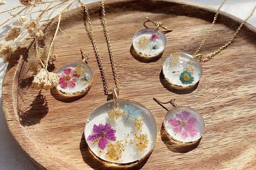 Una bandeja de madera con varios collares colgantes que tienen resina transparente con flores incrustadas. 4