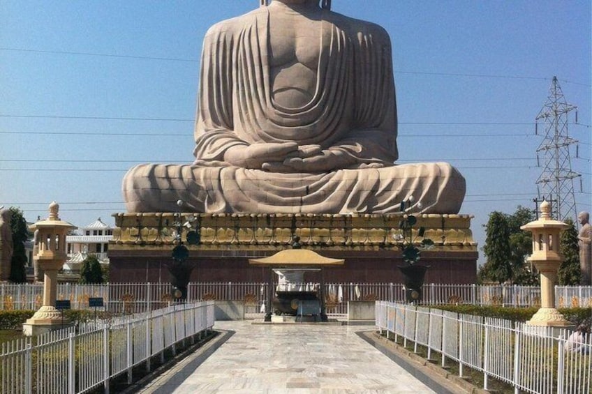 A large seated Buddha statue in a courtyard with a white fence and a lamp post. 4