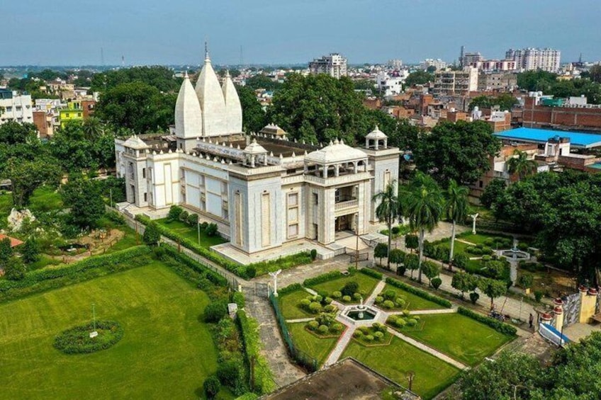 A large white temple with three domes, surrounded by well-maintained gardens and a cityscape in the background. 2