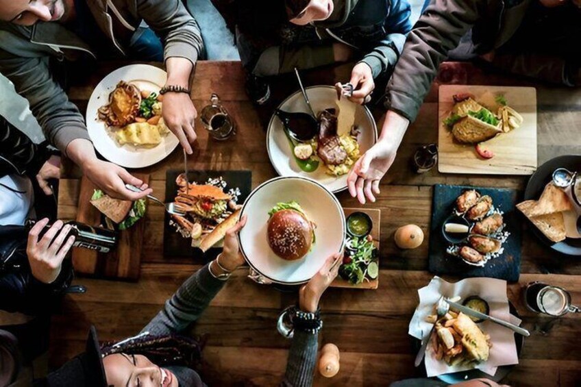 Un groupe de personnes est assis autour d’une table en bois et déguste différents plats, notamment des hamburgers, des salades et un steak. 5