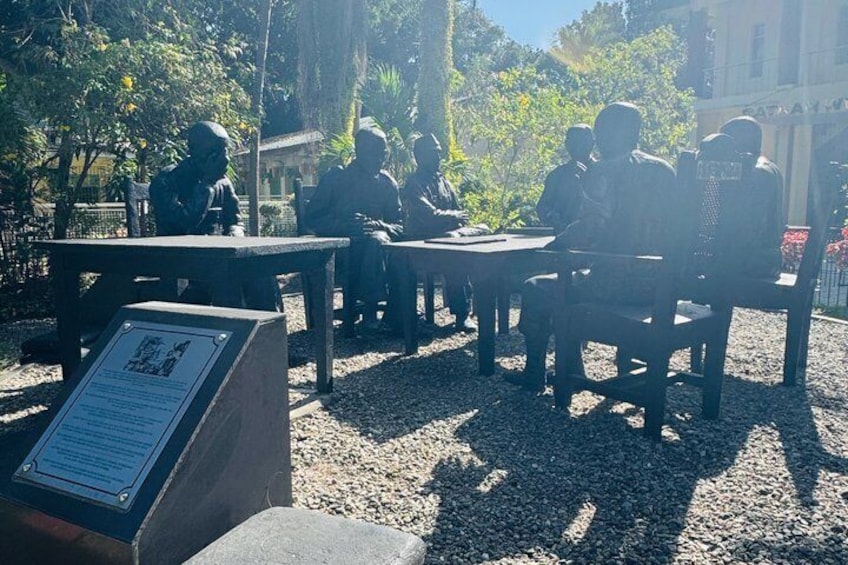 A group of people seated at tables in an outdoor setting with a plaque in the foreground. 3