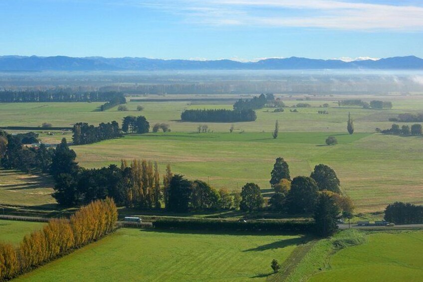 A vast rural landscape with rolling fields, scattered trees, and distant mountains under a clear sky. 4