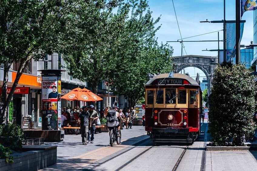 A trolley on tracks, people walking, and a bridge in the background. 2
