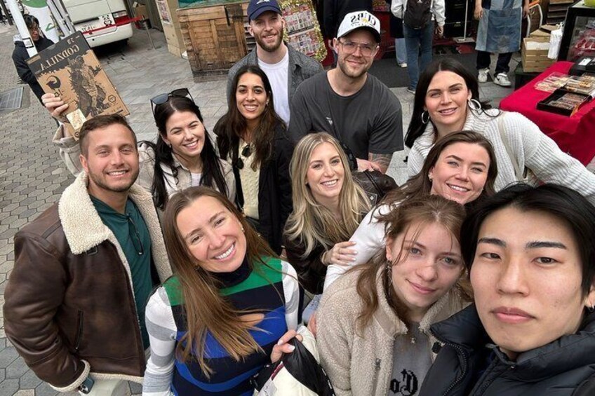Un grupo de personas posando para una foto en un mercado al aire libre con puestos de comida al fondo. 1