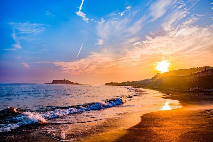 Ein Strand bei Sonnenuntergang mit Wellen, einer entfernten Insel und einem klaren Himmel. 2