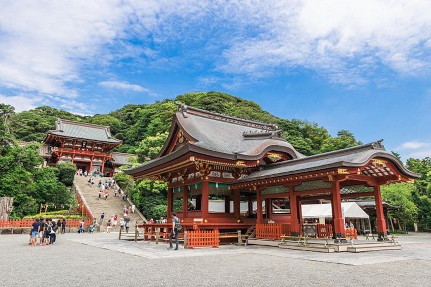 Ein traditioneller japanischer Tempel mit rotem Dach und Holzbau, umgeben von üppiger Vegetation und blauem Himmel. 4